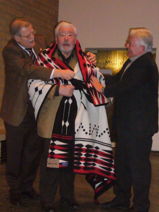 Volkmar Schultz (l) und Klaus Fischer (l) legen dem „Ehrenindianer“ Norbert Burger die Stammesdecke der Miami Indianer um.